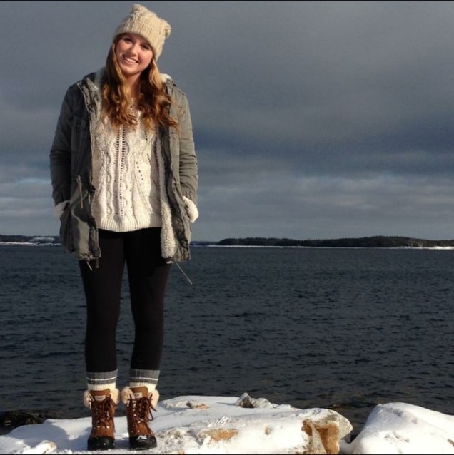 Beth MacDonald standing on a snowy rock in front of the ocean.